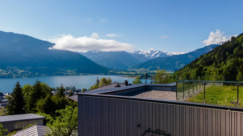 Moderner Bau mit Seeblick und Alpenpanorama unter blauem Himmel.