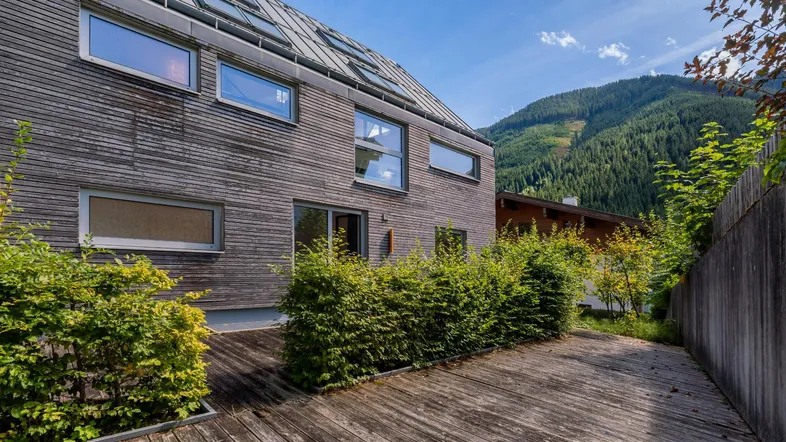 Moderne Holzfassade mit großer Holzterrasse und Blick auf die umliegenden Berge.