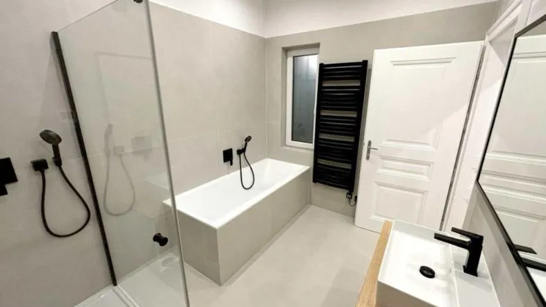 Modernes Badezimmer mit Badewanne, ebenerdiger Dusche, schwarzer Armatur und beheiztem Handtuchhalter.