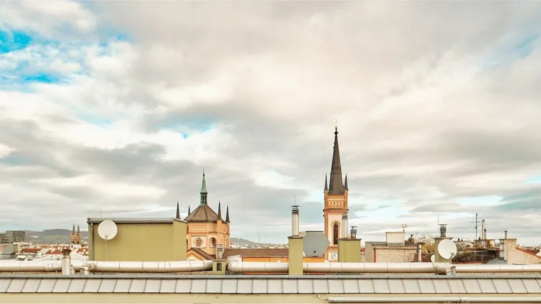 Panoramablick über die Dächer der Stadt mit historischen Kirchtürmen unter bewölktem Himmel.