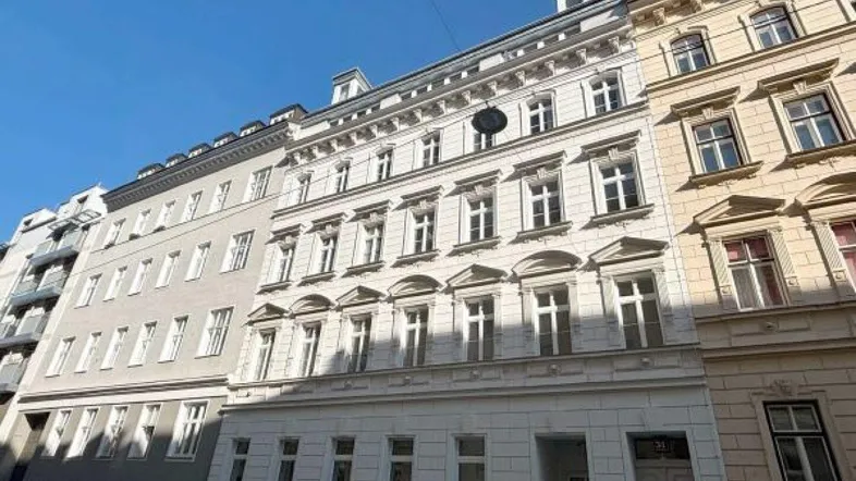 Weiß gestrichene Fassade eines Mehrfamilienhauses mit vielen Fenstern und klassischer Architektur in urbaner Umgebung.