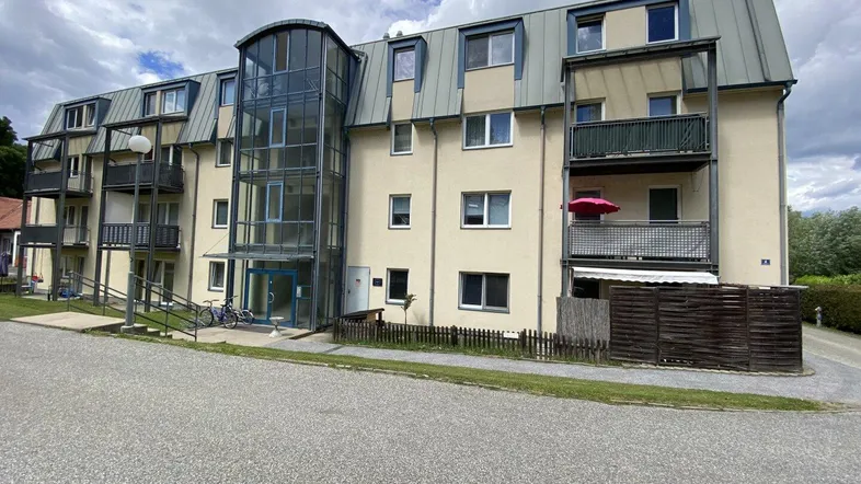 Mehrstöckiges Apartmentgebäude mit beiger Fassade, Balkonen und einem modernen Glasaufzug.