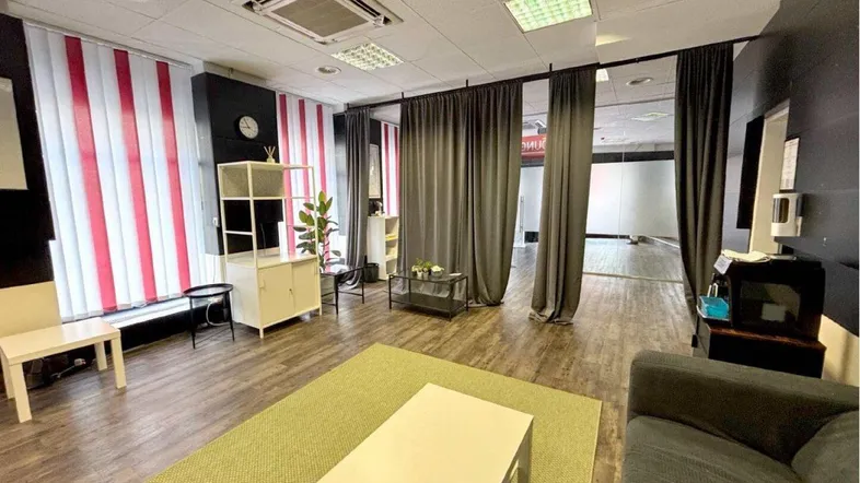 Geräumiger Innenbereich eines Büros oder einer Lounge mit Holzboden, modernen Möbeln und Vorhängen zur Raumteilung.
