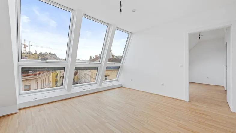 Heller Wohnraum im Dachgeschoss mit schrägen Fenstern und Blick auf die Stadt.