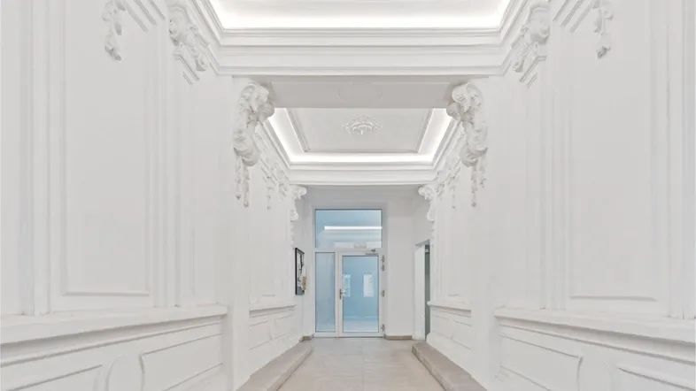 Eleganter, heller Flur mit aufwendigen Stuckverzierungen an Decke und Wänden, der zu einer Glastür führt.