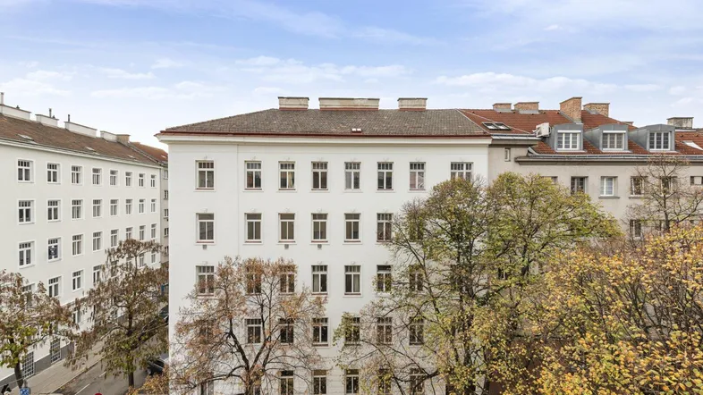 Mehrere Gebäude in einer städtischen Umgebung mit Bäumen und blauem Himmel.