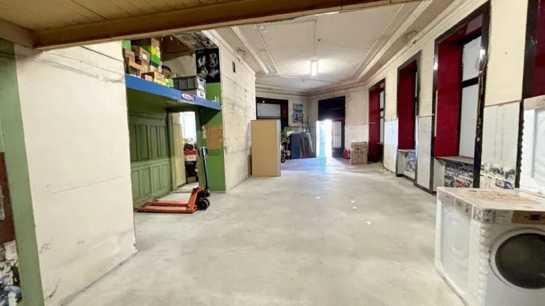 Geräumiger Gewerberaum mit Betonboden, hohen Decken und sichtbaren Lagerregalen.