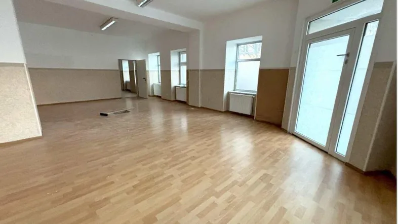 Geräumiger, leerer Gewerberaum mit hellem Laminatboden und mehreren Fenstern, bereit zur individuellen Gestaltung.
