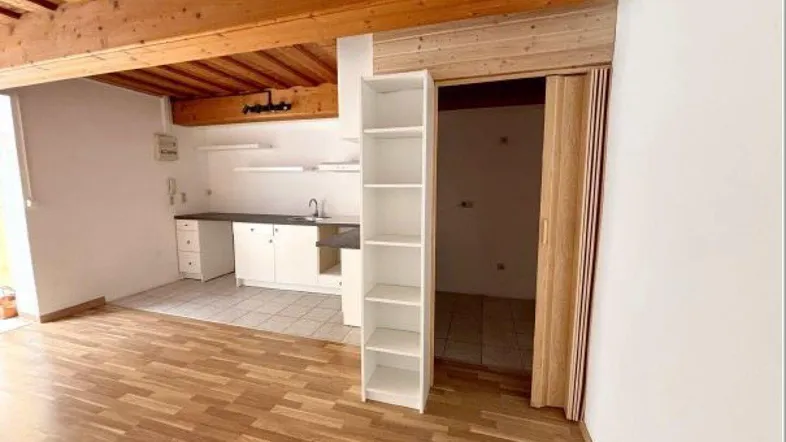 Offener Wohnbereich mit Holzbalkendecke, Laminatboden und einer einfachen Küchenzeile.