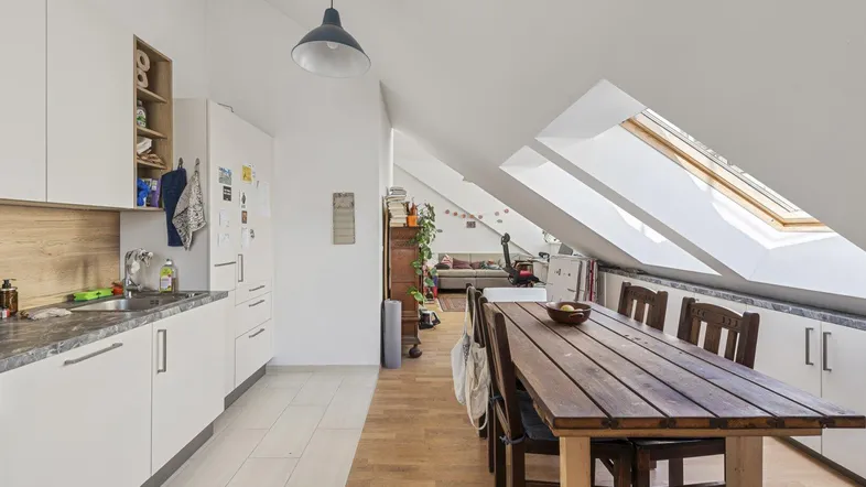 Helle Küche und Essbereich in einer Dachgeschosswohnung mit schrägen Decken und Holztisch.