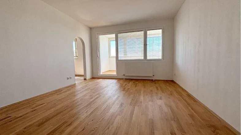 Helles Wohnzimmer mit Parkettboden und Zugang zu einem kleinen Balkon oder Wintergarten.