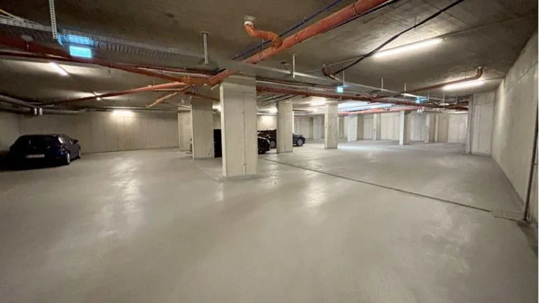 Geräumige Tiefgarage mit Betonstützen und sichtbaren Installationen, gut beleuchtet.