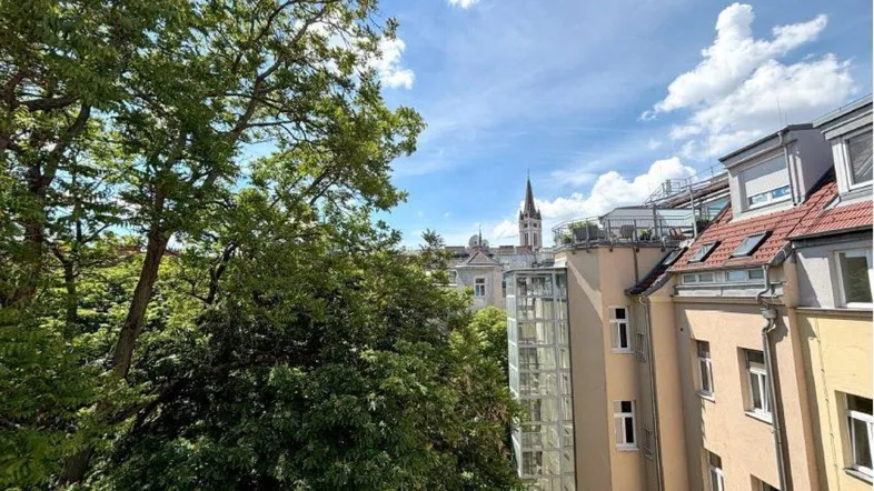 Blick von oben auf die umliegenden Gebäude, grüne Bäume und einen Kirchturm unter blauem Himmel.