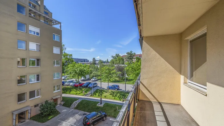 Blick vom Balkon auf den Innenhof mit Parkplätzen, umgeben von Bäumen und weiteren Wohngebäuden.