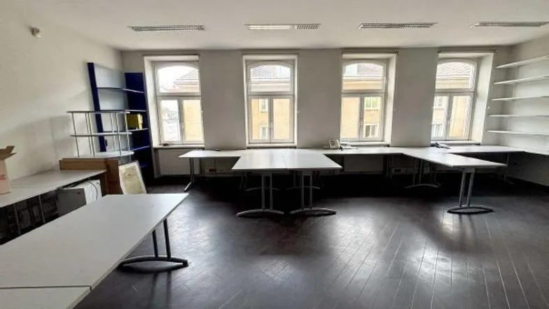 Geräumiges Büro mit mehreren Arbeitsplätzen, großen Fenstern und dunklem Holzboden.