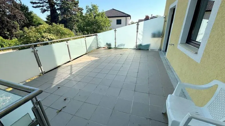 Große geflieste Terrasse mit Milchglasgeländer und Blick ins Grüne, ideal zum Entspannen.