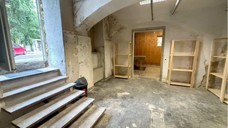 Geräumiger Lagerraum mit Betonboden, rohen Wänden und Zugang zu weiteren Räumen sowie zur Straße.