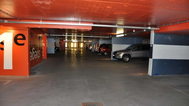 Geräumige Tiefgarage mit mehreren Stellplätzen, orangefarbenen Wänden und Betonboden.