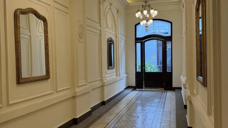 Langer Flur mit eleganten Kronleuchtern, verzierten Decken und gemusterten Fliesenböden, der zum Eingang führt.