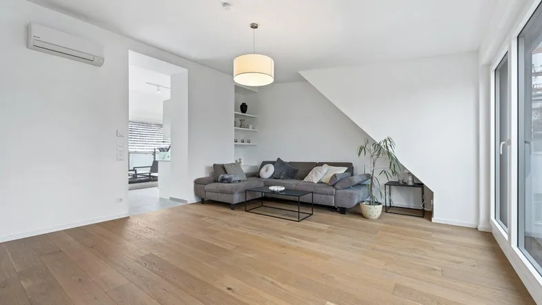 Helles Wohnzimmer mit Holzboden, bequemer Couch und Zugang zu einem weiteren Bereich.