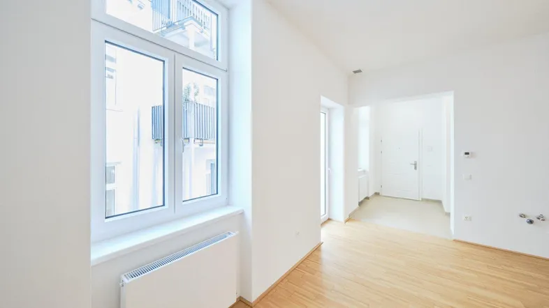 Helles, leeres Zimmer mit Parkettboden und großem Fenster, das einen Blick auf den Innenhof bietet.