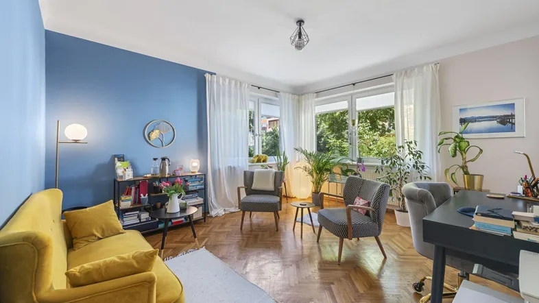 Helles Wohnzimmer mit blauer Akzentwand, gelbem Sofa und Fischgrätparkettboden.