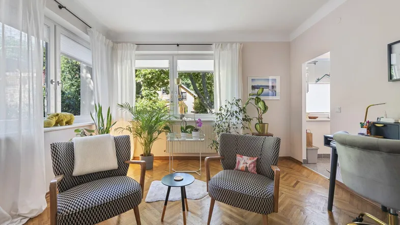 Helles Wohnzimmer mit Fischgrätparkett, vielen Pflanzen und einem Arbeitsbereich am Fenster.