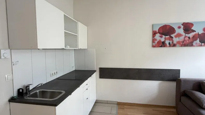 Helle Küchenzeile mit weißen Schränken und angrenzendem Wohnbereich mit Holzboden.