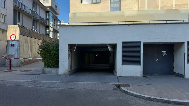 Eingang zu einer modernen Tiefgarage mit Schranke und Zufahrtsrampe in einem Neubau.