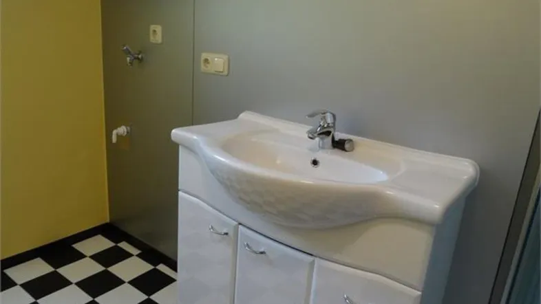 Badezimmer mit Waschbecken, Unterschrank und auffälligem schwarz-weiß kariertem Boden.