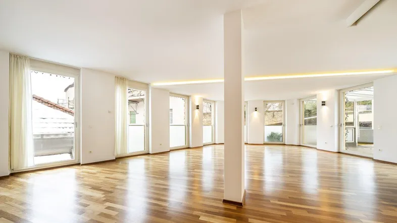 Helles, offenes Wohnzimmer mit Parkettboden und vielen Fenstern, die Zugang zu Balkonen bieten.