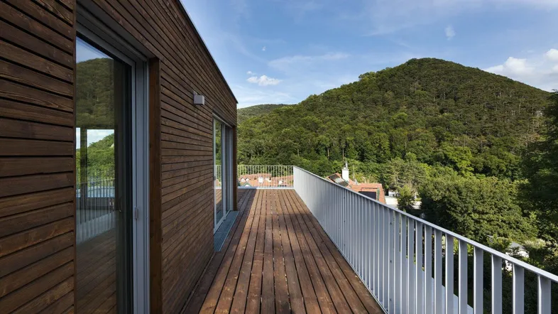 Geräumige Holzterrasse mit weißem Geländer und weitem Blick auf bewaldete Hügel.