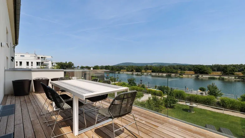 Große Holzterrasse mit Esstisch und Stühlen, bietet einen weiten Blick auf den See und die umliegende Landschaft.