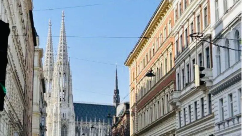 Historische Stadtansicht mit Gebäuden, parkenden Autos und einer Kirche im Hintergrund.