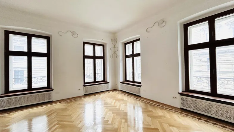 Helles, leeres Zimmer mit Fischgrätparkett und großen Fenstern.