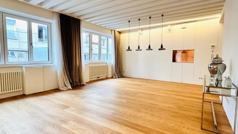 Helles Wohnzimmer mit Holzboden, sichtbaren Deckenbalken und großen Fenstern.