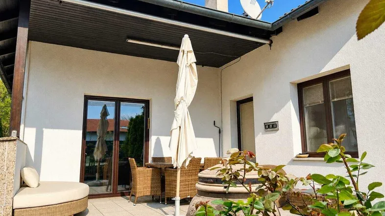 Geräumige Terrasse mit Sitzgelegenheiten, Sonnenschirm und Blick ins Grüne an einem sonnigen Tag.
