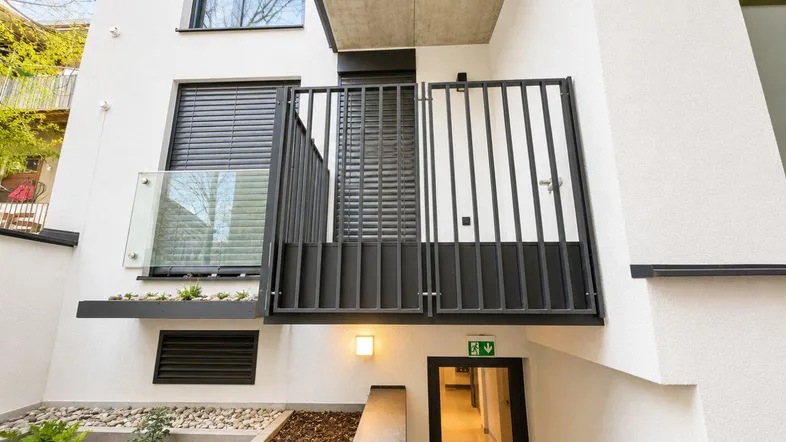 Moderner Gebäudeeingangsbereich mit kleinem Balkon und Zugang zu den Wohneinheiten.