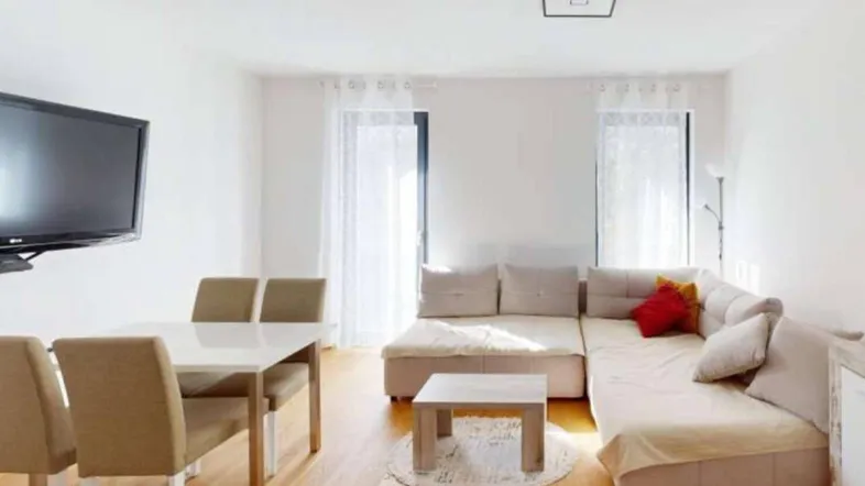 Heller Wohn- und Essbereich mit modernem Sofa, Esstisch und Zugang zu den Fenstern.