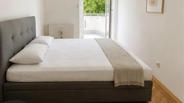 Gemütliches Schlafzimmer mit Parkettboden und direktem Zugang zu einem sonnigen Balkon.