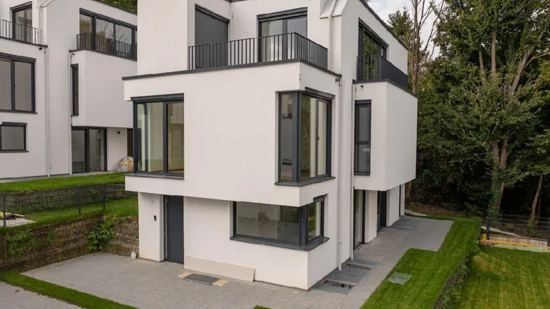 Moderne weiße Architektur mit großen Fenstern, Balkonen und umgebenden Grünflächen in einer ruhigen Lage.