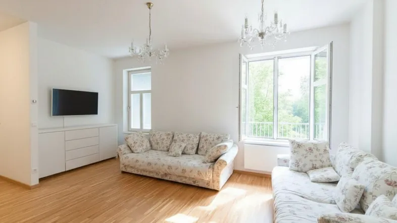 Geräumiges Wohnzimmer mit hellen Wänden, Holzboden und großen Fenstern, die viel Tageslicht hereinlassen.