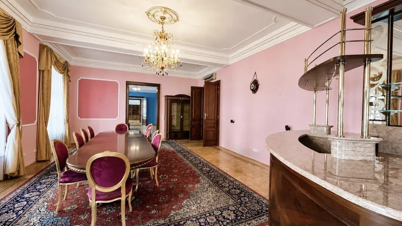 Elegantes Esszimmer mit rosafarbenen Wänden, Stuckdecke, Kronleuchter und einer integrierten Bar.