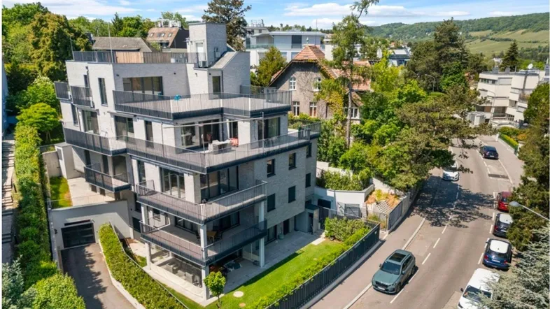 Moderne Wohnanlage mit mehreren Balkonen und Terrassen, umgeben von viel Grün und einer Straße.