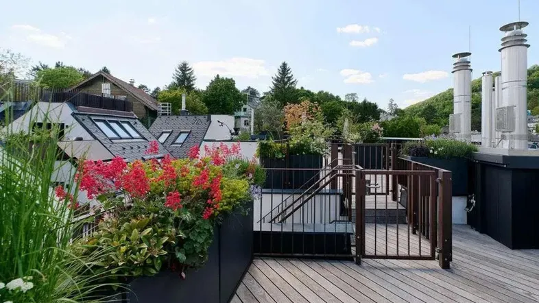 Geräumige Dachterrasse mit Holzbelag, Blumenbeeten und Blick auf die umliegende Bebauung und Natur.