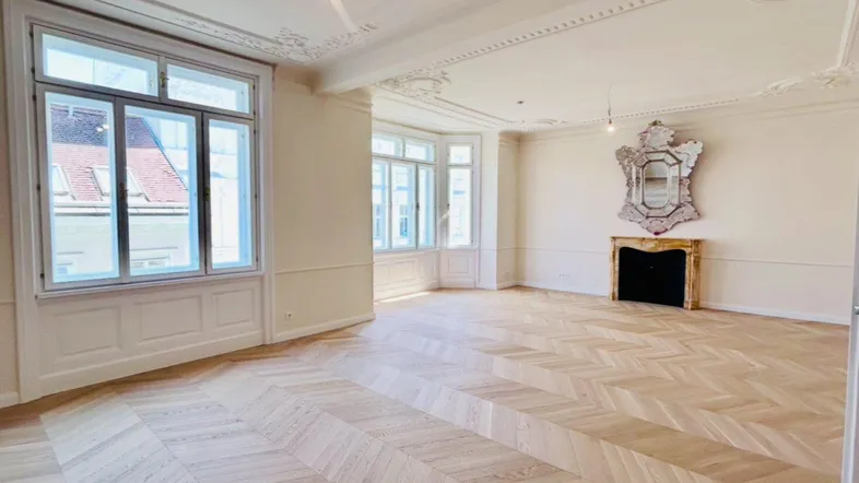 Helles Wohnzimmer mit elegantem Fischgrätparkett, hohen Decken und klassischem Kamin in einem Altbau.
