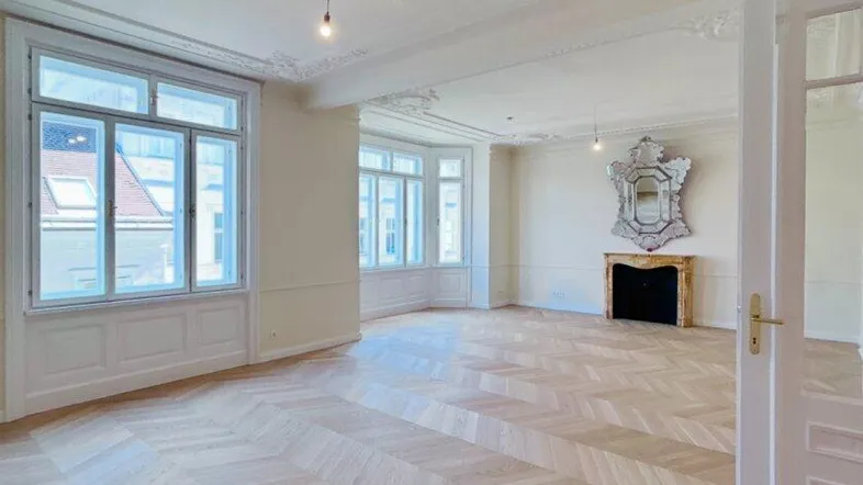Großzügiges Wohnzimmer mit Fischgrätparkett, Stuckdecken und einem dekorativen Kamin in einem Altbau.