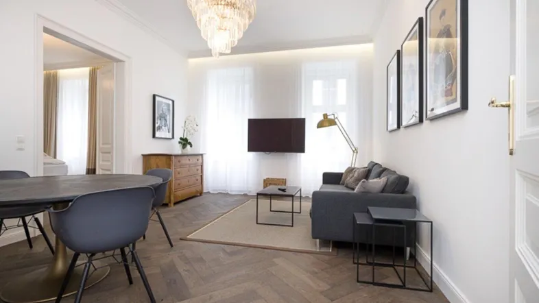 Heller Wohn- und Essbereich mit Fischgrätparkett, modernem Sofa und elegantem Kronleuchter.