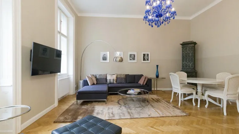 Geräumiger Wohn-Essbereich mit Fischgrätparkett, modernem Sofa, Kachelofen und blauem Kronleuchter.