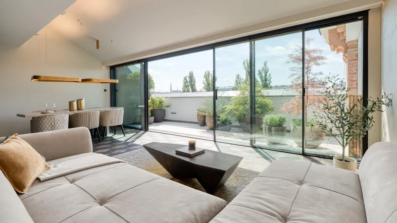 Geräumiges Wohnzimmer mit großen Glasfronten, die den Blick auf die Terrasse und die Stadt freigeben.